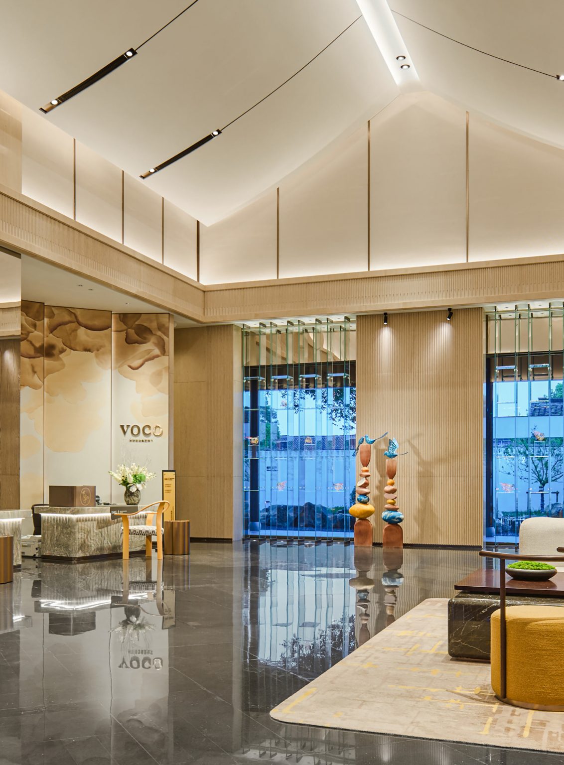 Spacious hotel lobby with modern design features a high ceiling, artistic wall panel, sleek reception desk, and elegant seating, conveying a luxurious ambiance.