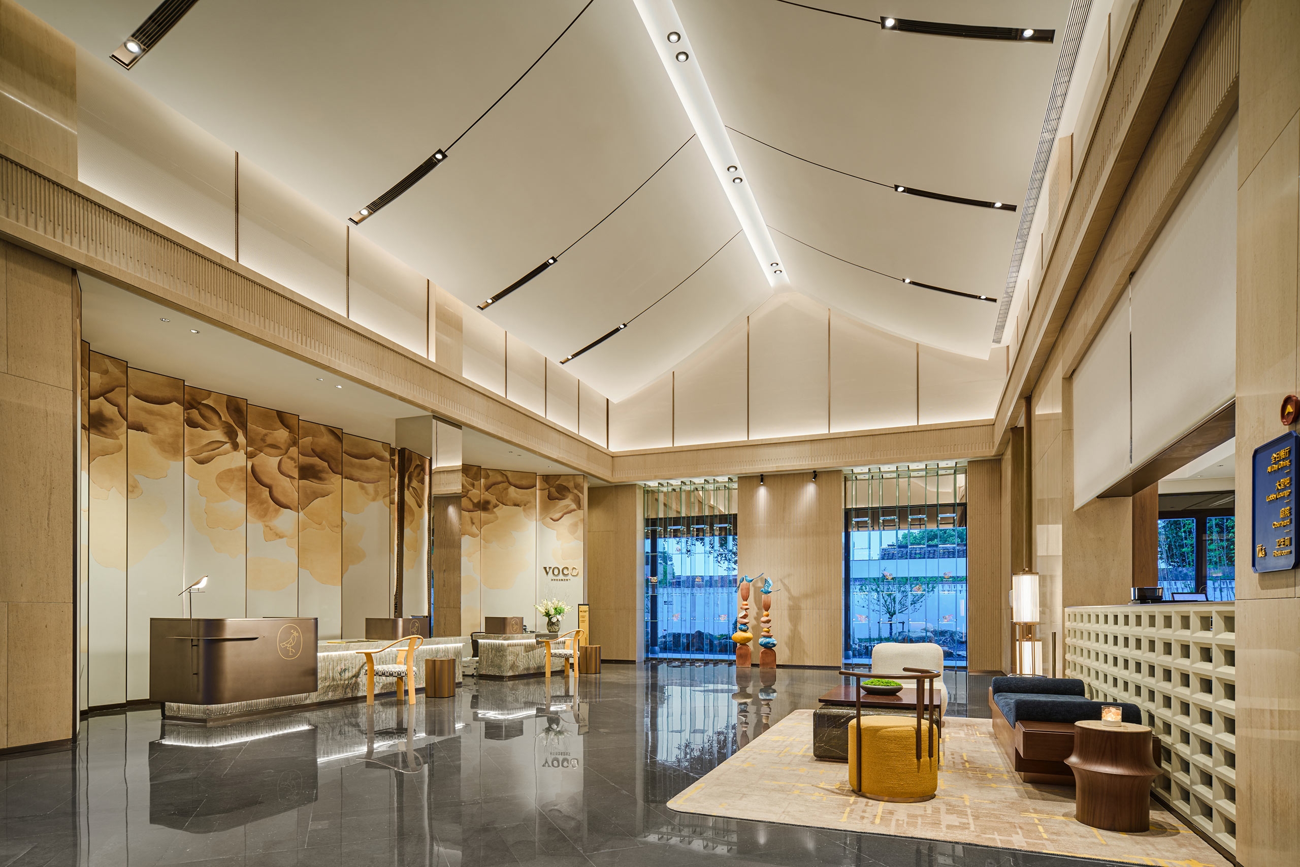 Spacious hotel lobby with modern design features a high ceiling, artistic wall panel, sleek reception desk, and elegant seating, conveying a luxurious ambiance.