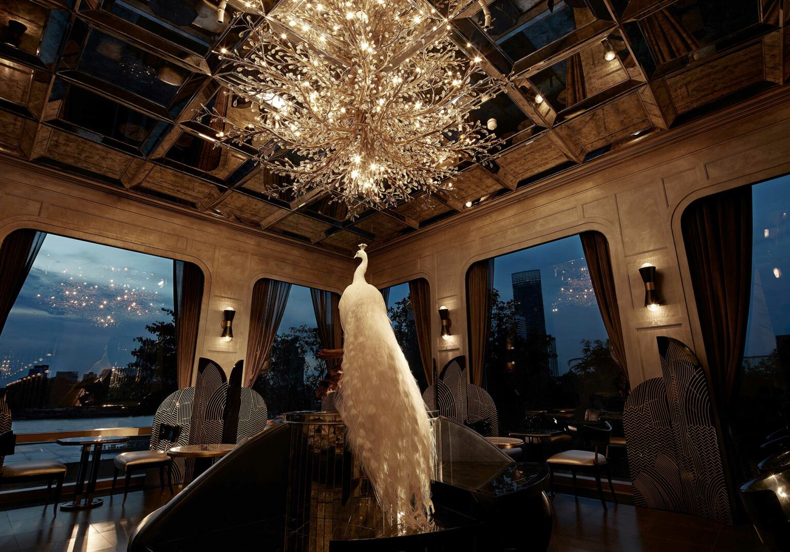 Elegant cocktail salon with a large, crystal chandelier resembling a tree, a white peacock sculpture beneath it. Evening city view through tall windows. Luxurious atmosphere.