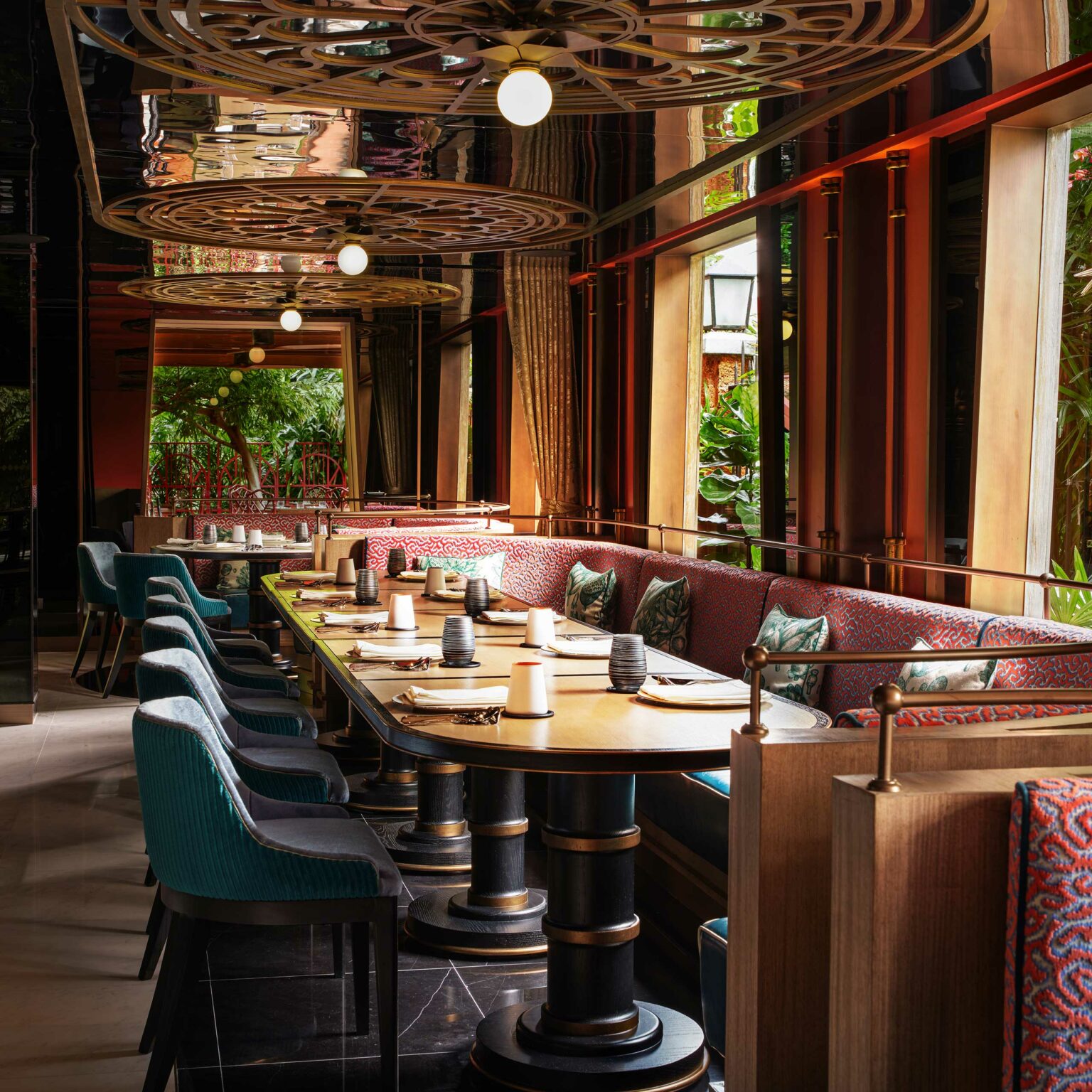 Elegant restaurant interior with a long table set for dining, surrounded by teal chairs and red cushioned benches. Mood lighting and decorative ceiling panels enhance the sophisticated ambiance.
