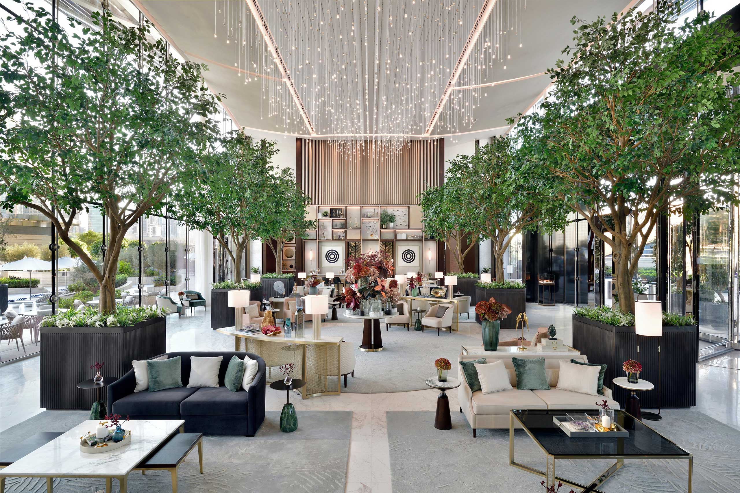 Luxurious hotel lobby with high ceiling and string lights. Features elegant sofas, coffee tables, and potted trees. Airy and sophisticated ambiance.