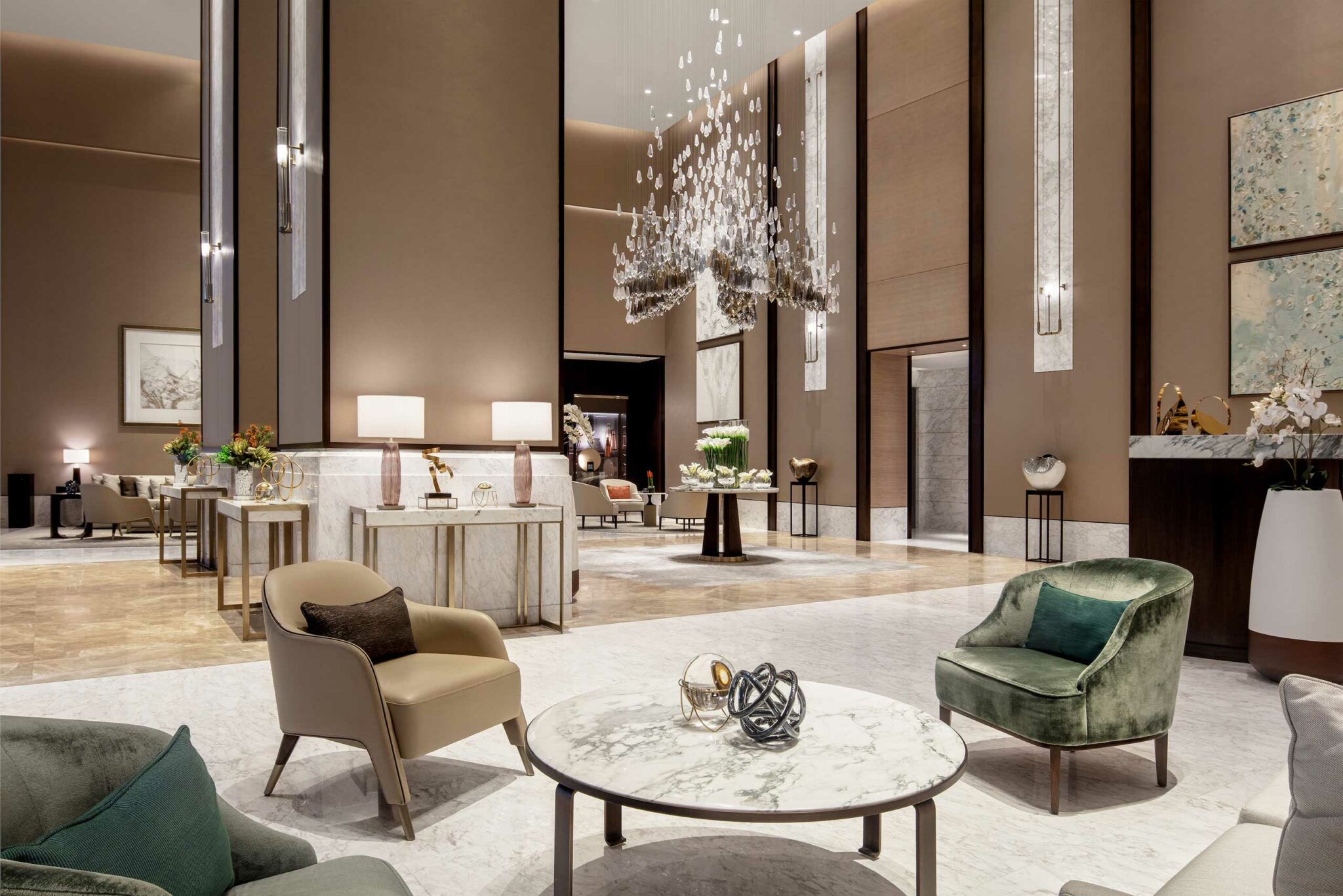 Luxurious hotel lobby with high ceilings, modern chandeliers, and elegant seating. Neutral tones and artwork create a sophisticated, welcoming atmosphere.
