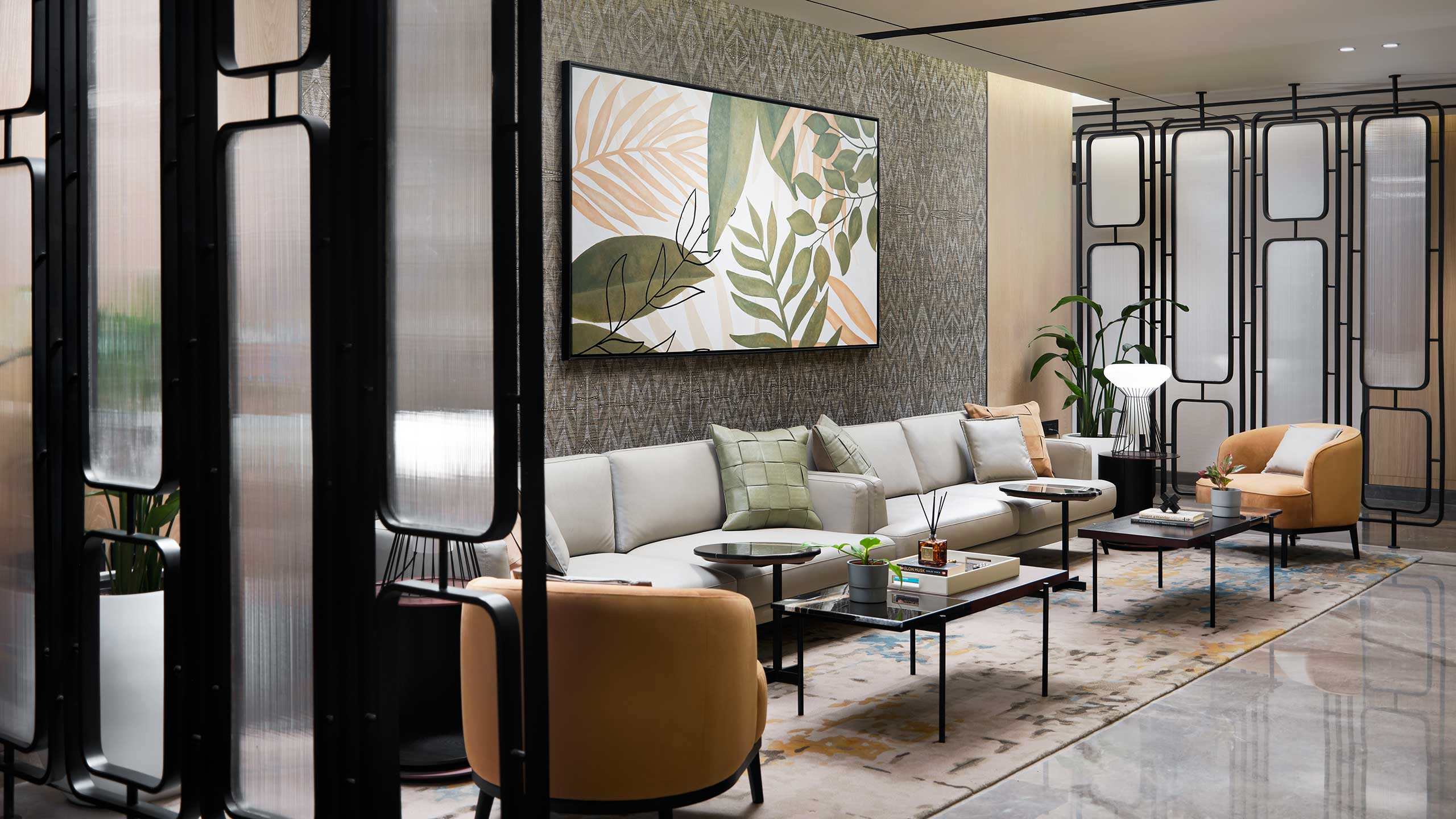 Modern office lounge with a neutral-toned sofa, yellow chairs, and abstract leaf art. Glass partition and soft lighting create an elegant, serene atmosphere.