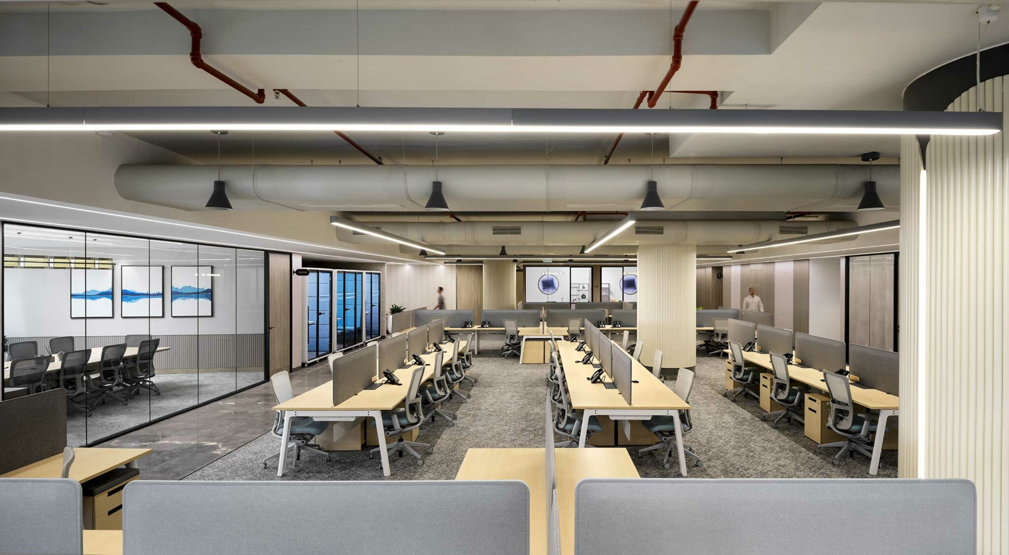 Modern open-plan office with neutral tones, featuring desks arranged in rows, ergonomic chairs, and minimalist decor. Glass-walled meeting room on the side.