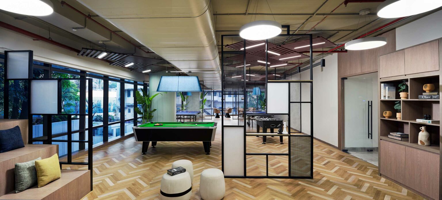 Modern office lounge with a pool table, foosball, and open seating. Large windows let in natural light, creating a relaxed, inviting atmosphere.