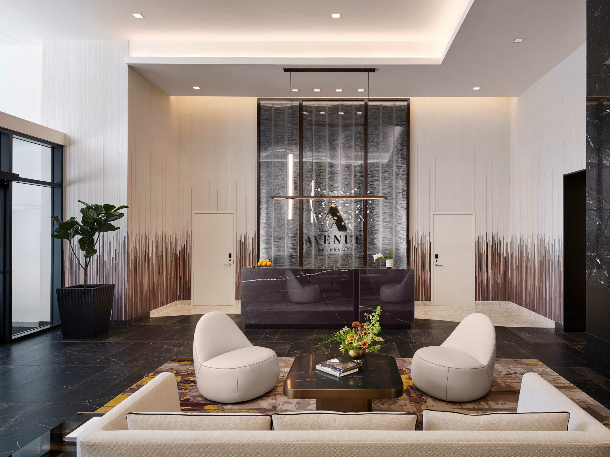 Luxurious hotel lobby featuring sleek modern design. Central reception desk with black marble and decorative lighting, surrounded by plush seating and plants.