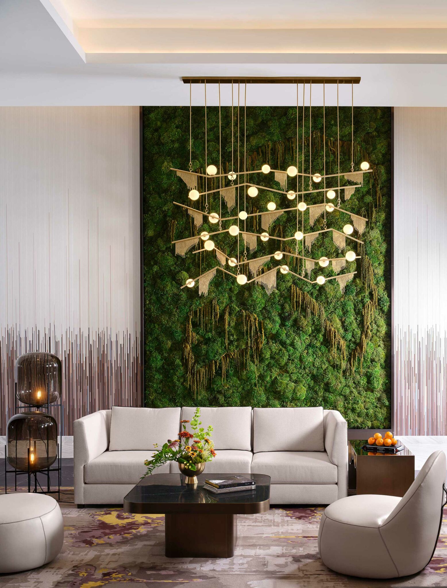 Modern hotel lounge with a large green moss wall, geometric chandelier, and sleek furniture. Cozy ambiance with a beige sofa, dark table, and decorative plants.