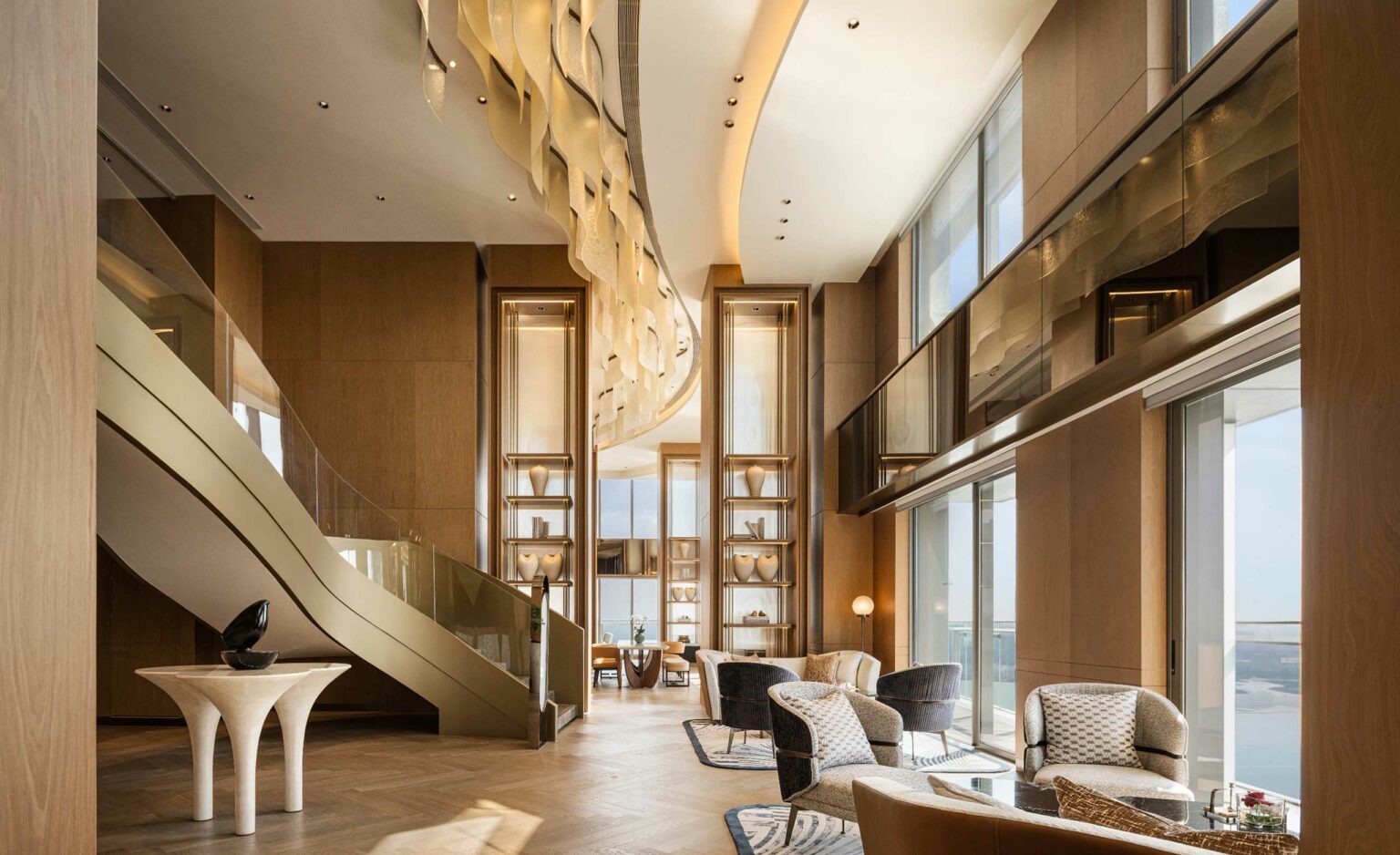 Luxurious modern hotel lounge with high ceilings, large windows, curved staircase, and elegant furniture. Warm tones create a sophisticated, inviting atmosphere.