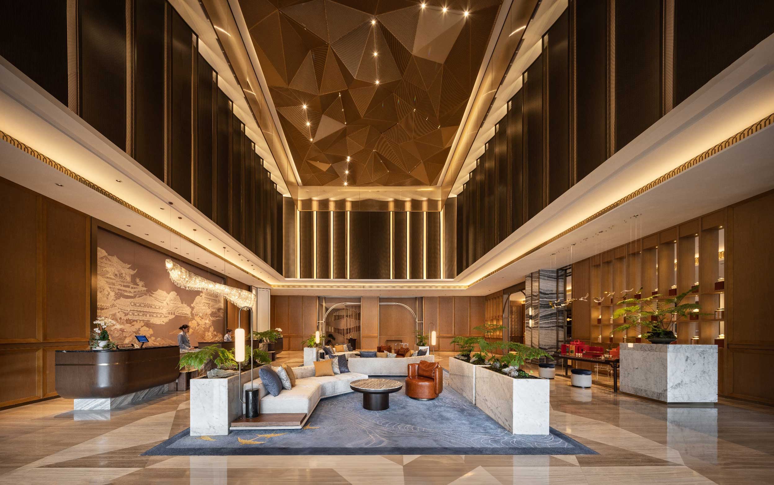 Luxurious hotel lobby with geometric ceiling, elegant lighting, modern seating, and indoor plants. Warm tones and sleek design create a welcoming atmosphere.