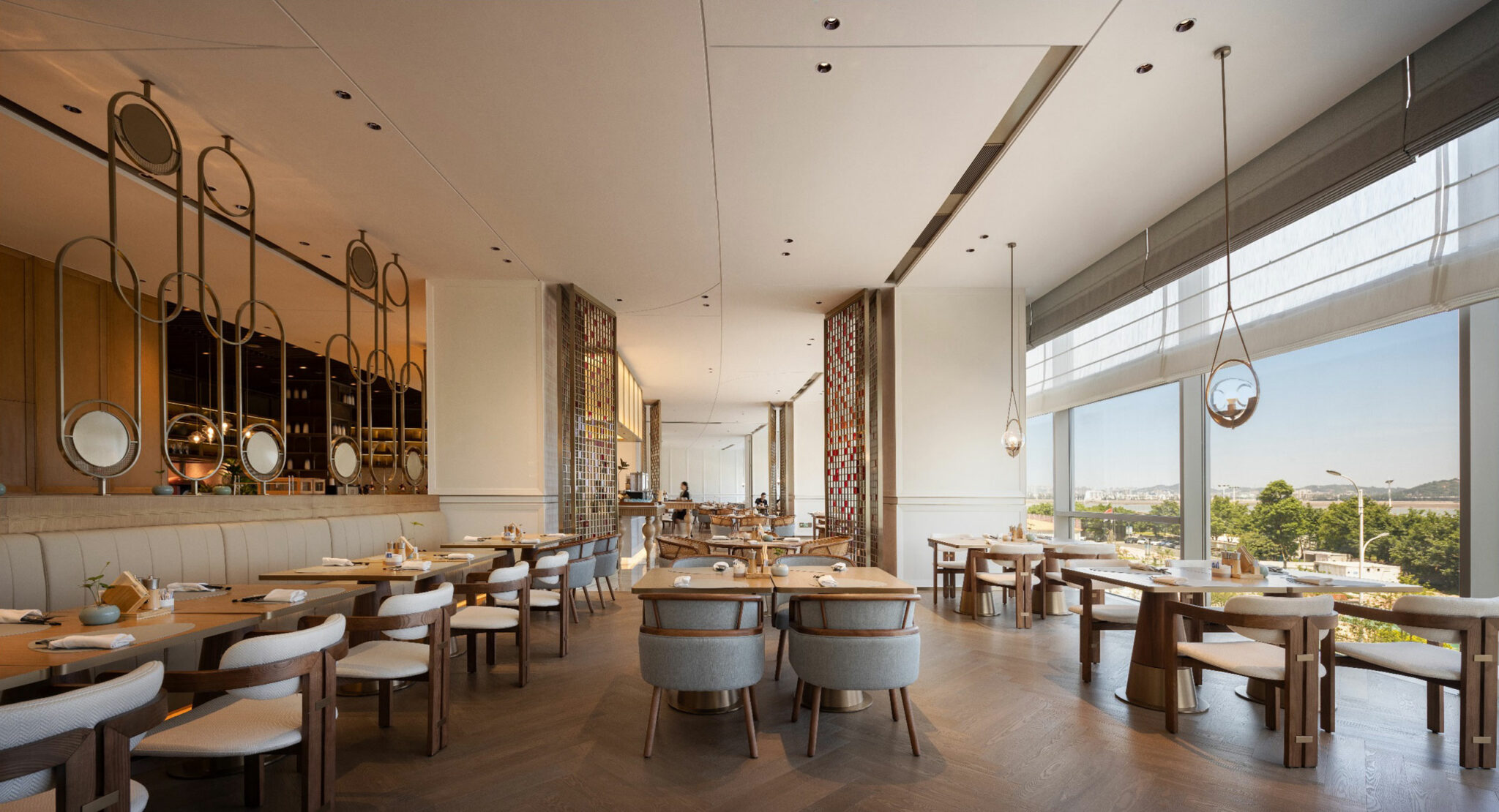 Spacious hotel restaurant interior with modern decor, featuring wooden tables and chairs, large windows with natural light, and decorative mirrors on the walls.