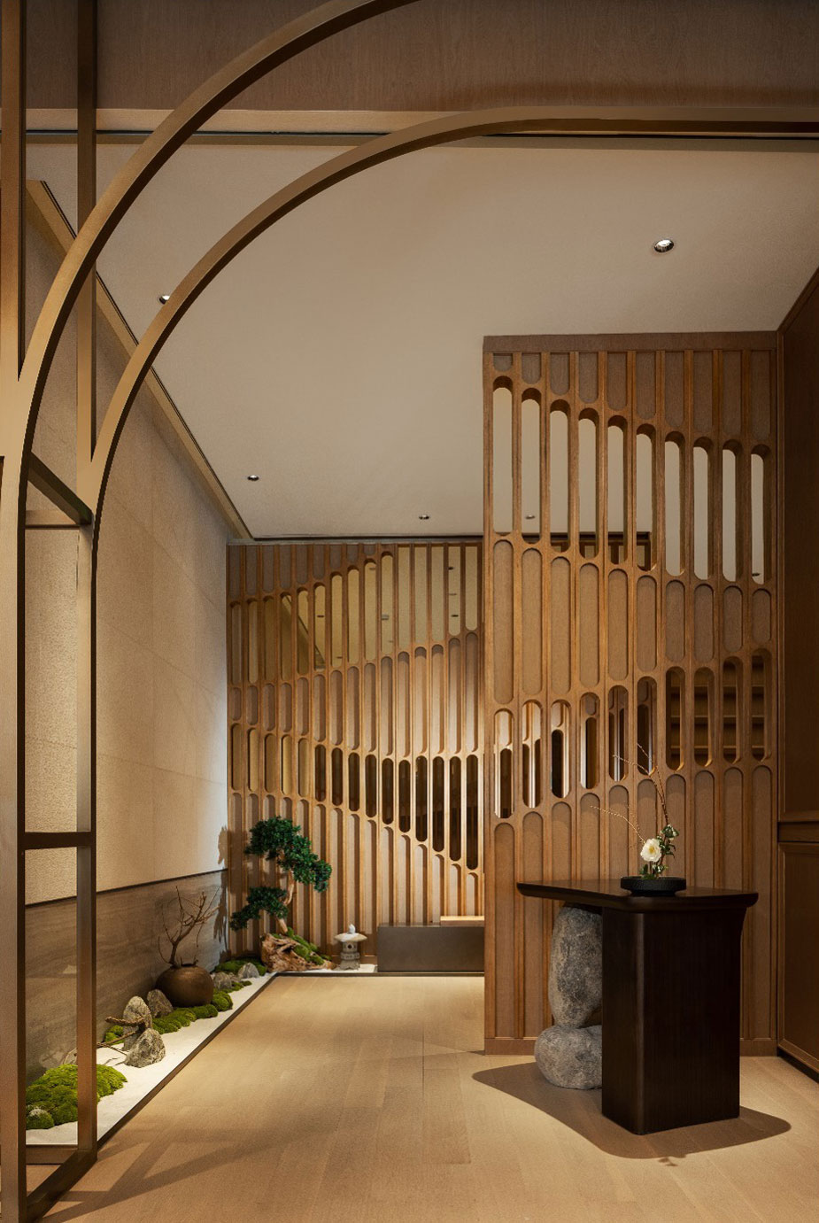 Elegant interior of a hotel restaurant reception area showcasing a minimalist Japanese design with wooden lattice dividers, a small rock garden, and a dark wooden table, conveying tranquility.