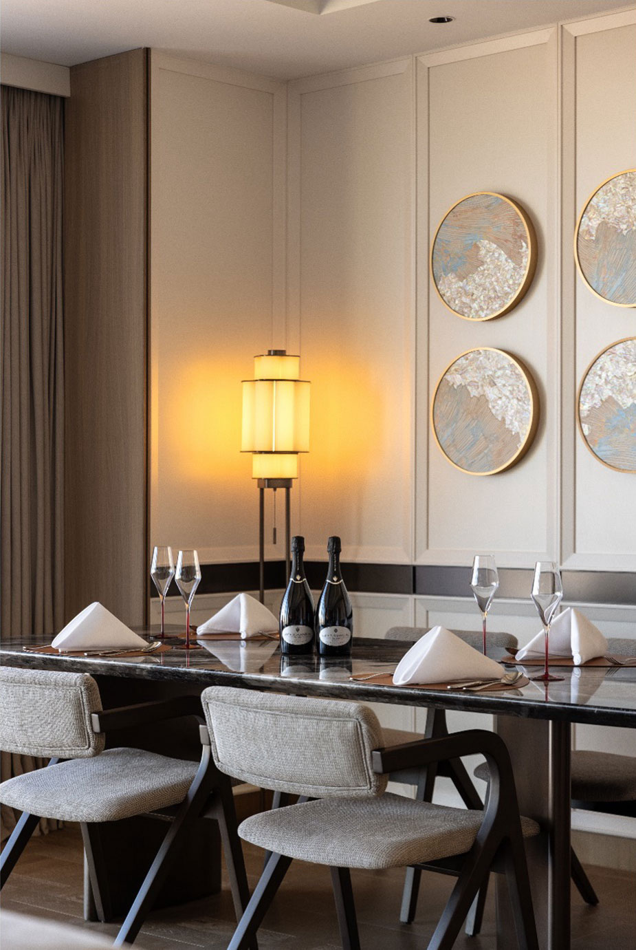 Elegant suite dining area with a dark marble table set for four, featuring folded napkins and wine glasses. Soft lighting and abstract wall art create a warm ambiance.