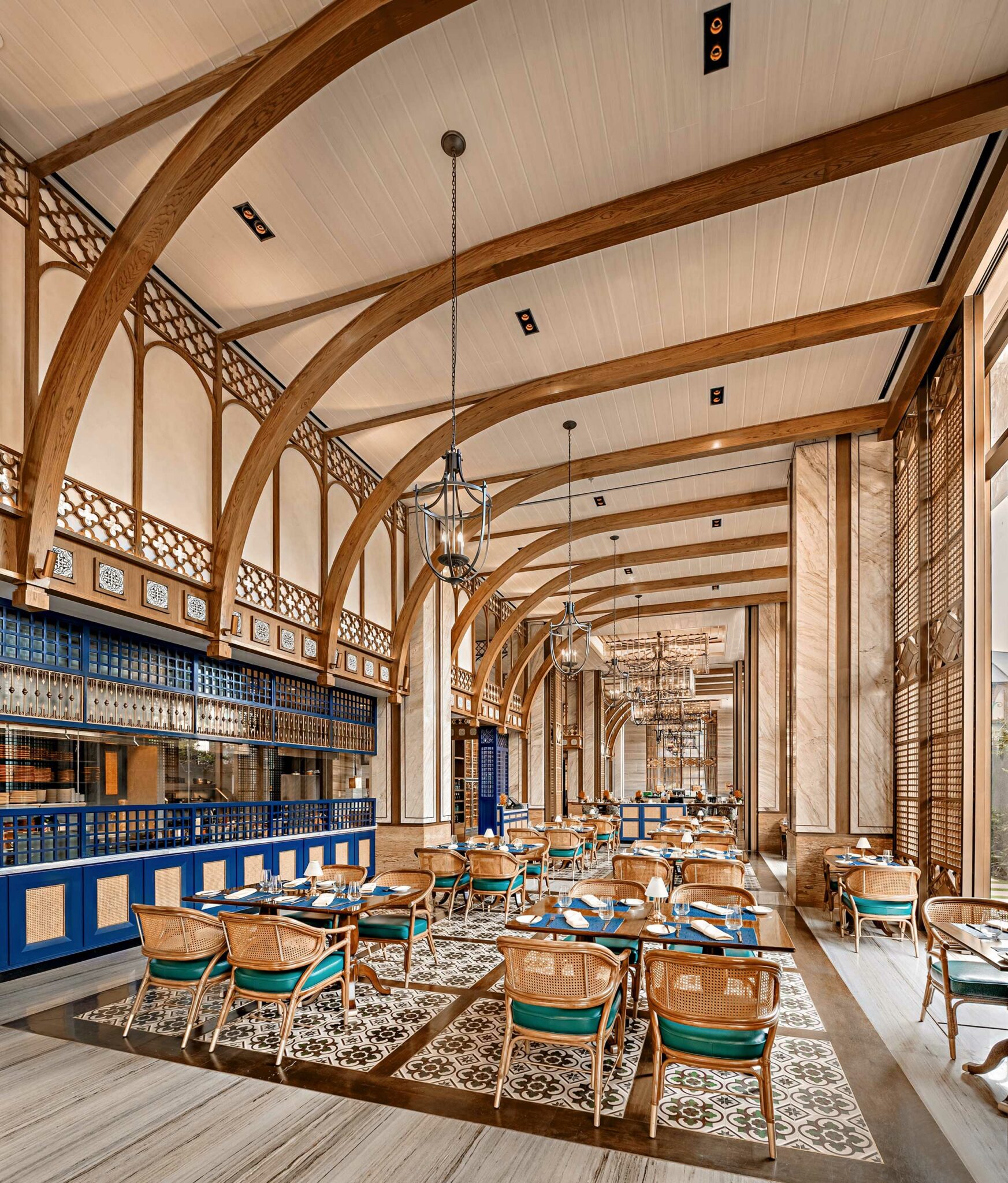 Elegant restaurant interior with arched wooden beams, patterned tile floor, and wicker chairs around dark tables. Warm lighting and intricate metalwork enhance the sophisticated ambiance.