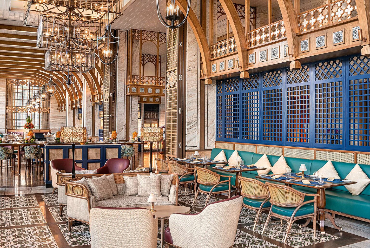 Luxurious restaurant interior with elegant chandeliers, arched wood ceilings, marble walls, and ornate blue lattice panels. Cozy seating and warm lighting.