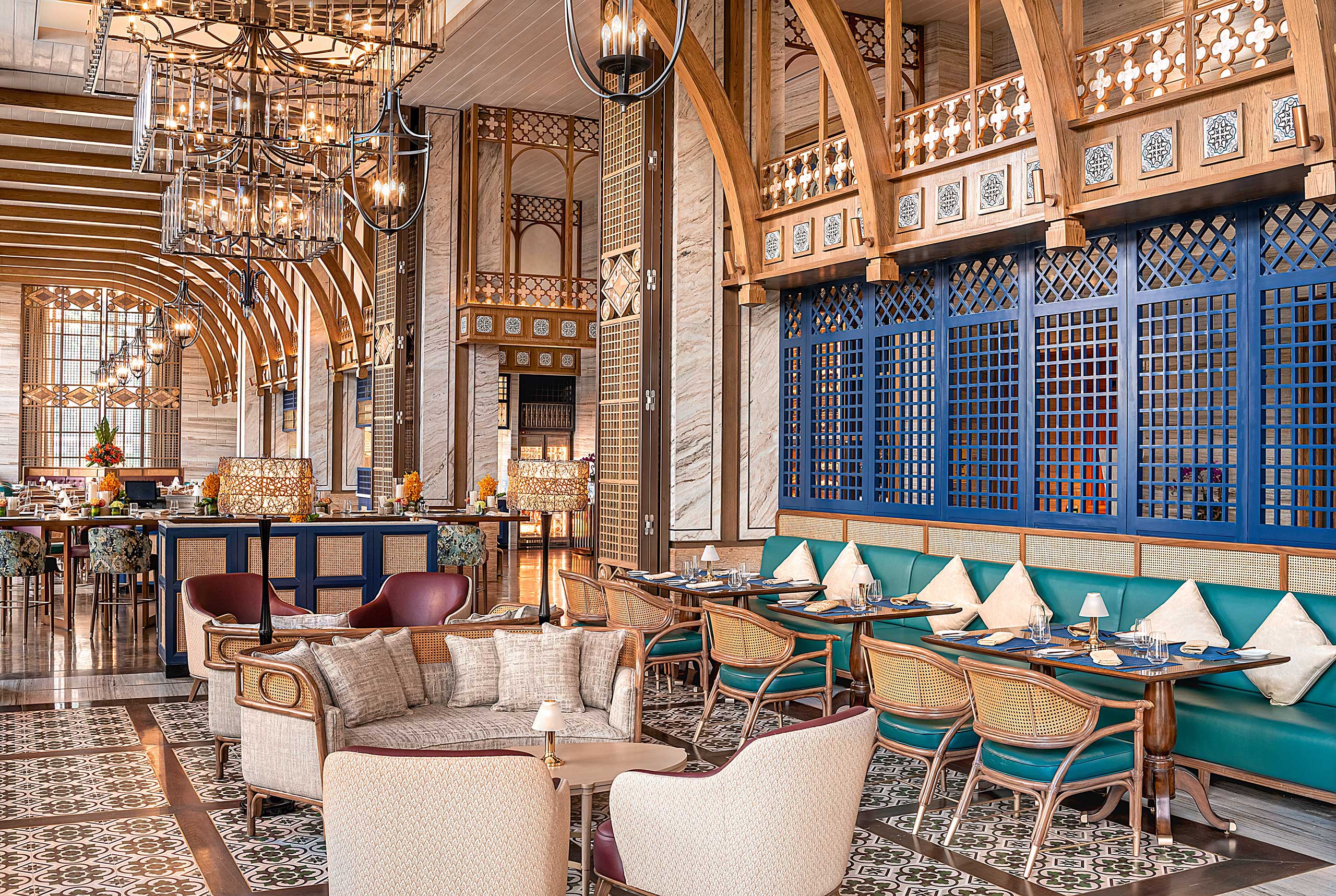 Luxurious restaurant interior with elegant chandeliers, arched wood ceilings, marble walls, and ornate blue lattice panels. Cozy seating and warm lighting.