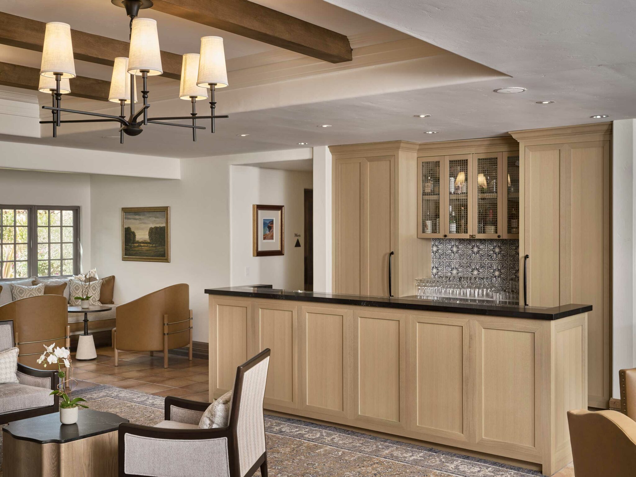 Sophisticated suite living area with light wood cabinetry, dark countertop, patterned backsplash, and elegant chandelier. Neutral tones create a warm, inviting ambiance.