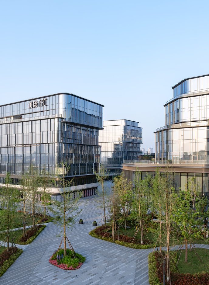 Modern commercial glass buildings with illuminated interiors stand amidst lush greenery under a dawn sky, evoking a sense of sophistication and calm.