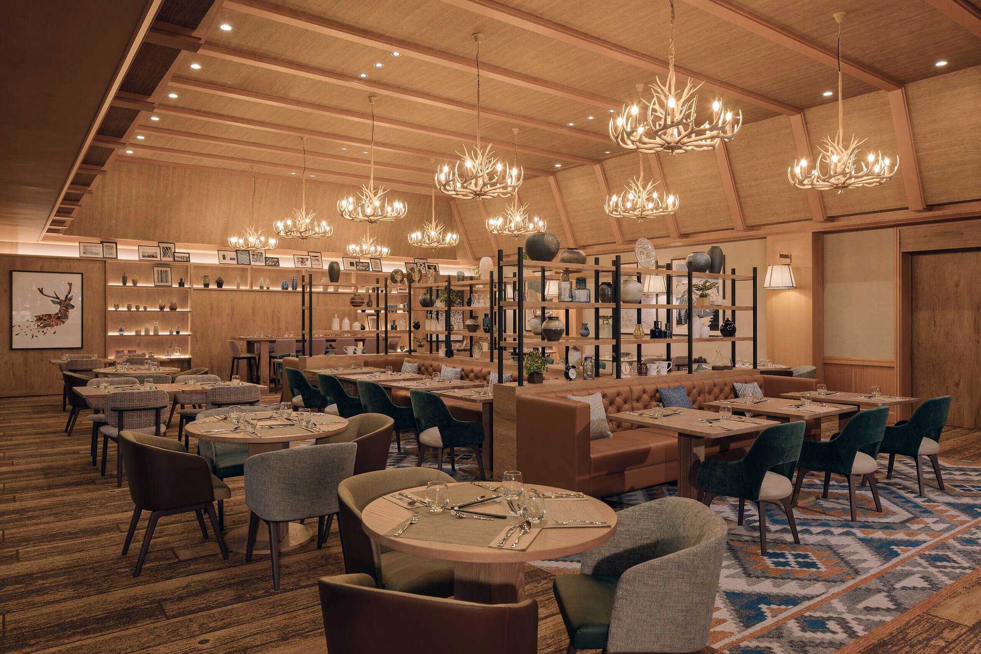 Spacious, elegant hotel restaurant interior with wooden ceilings and antler chandeliers. Round tables set with glassware, cushioned chairs, and warm ambiance.