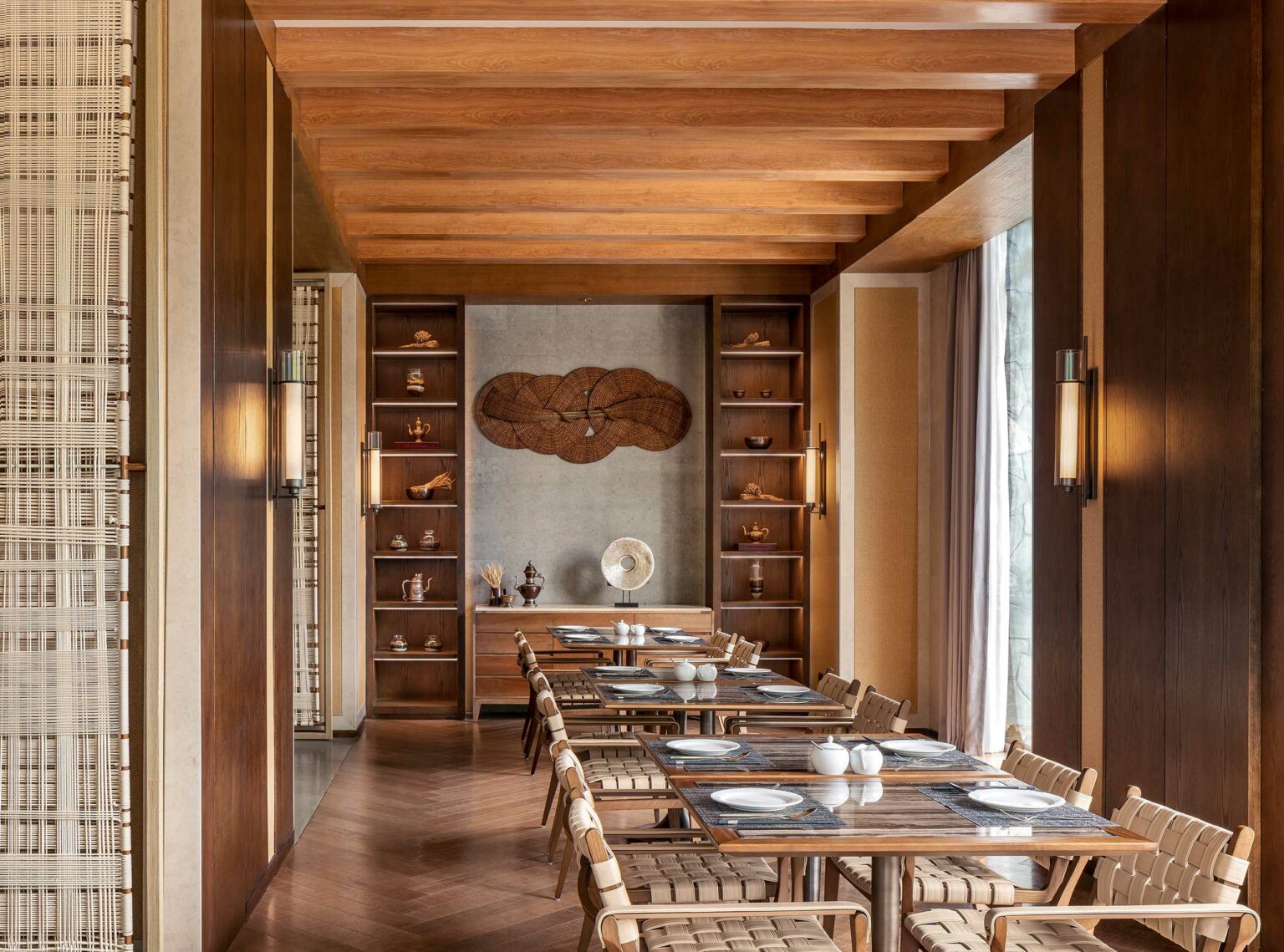 A sophisticated hotel dining room with wooden beams and shelves displaying art pieces. Elegant tables are set for dining, creating a warm and inviting atmosphere.