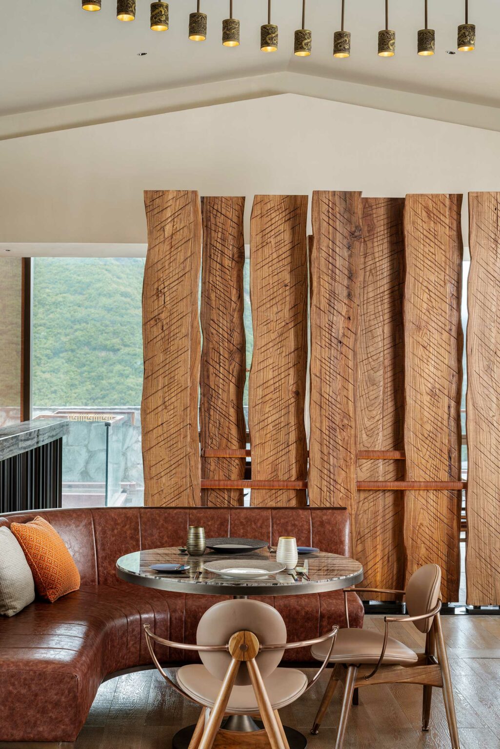 A hotel dining area features a curved leather bench with a round table set for two. Wooden vertical panels decorate the background, creating a warm, earthy ambiance.