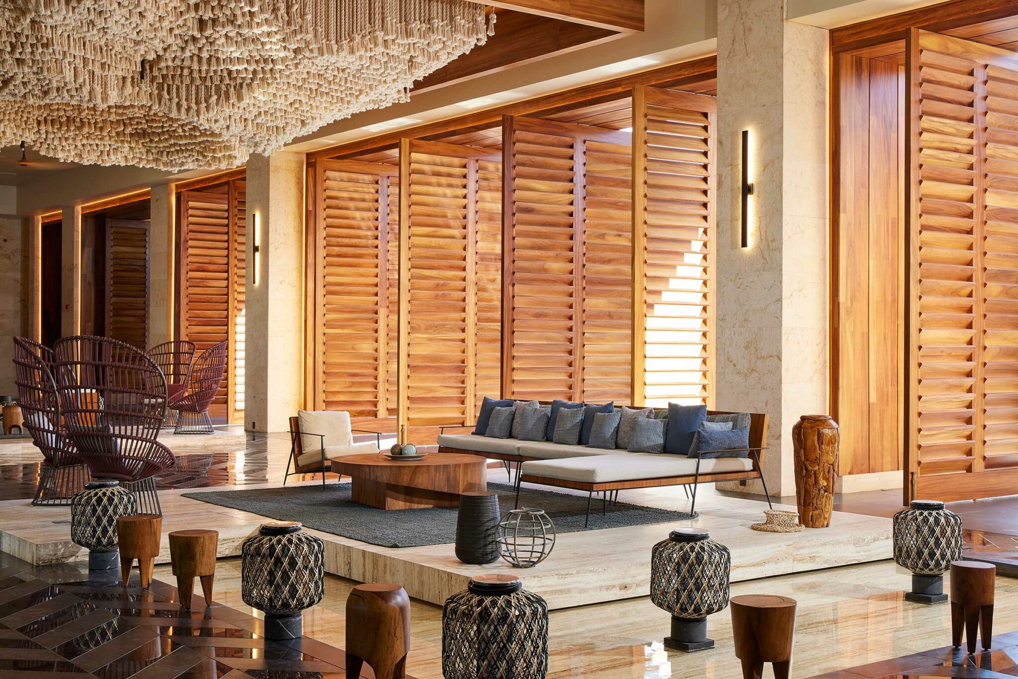 Luxurious resort lounge with wood panels, modern seating, and textured décor. Warm lighting and a large chandelier create a serene, inviting atmosphere.
