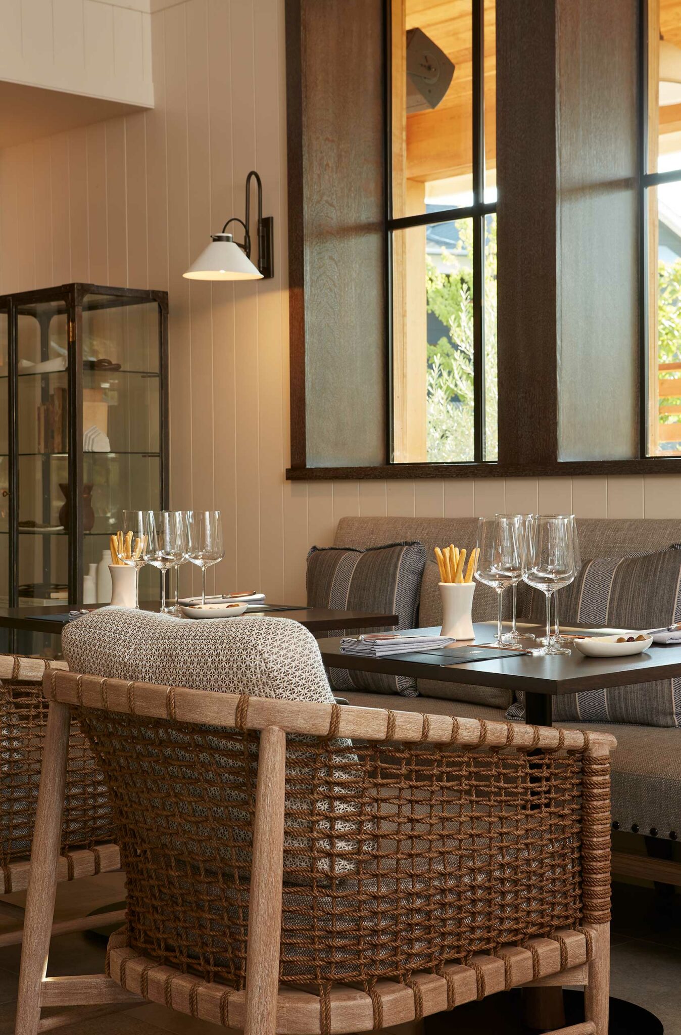 Cozy dining corner of a wine resort with a black table set for four. Glasses and cutlery arranged neatly. Soft beige and orange tones with modern art on walls.