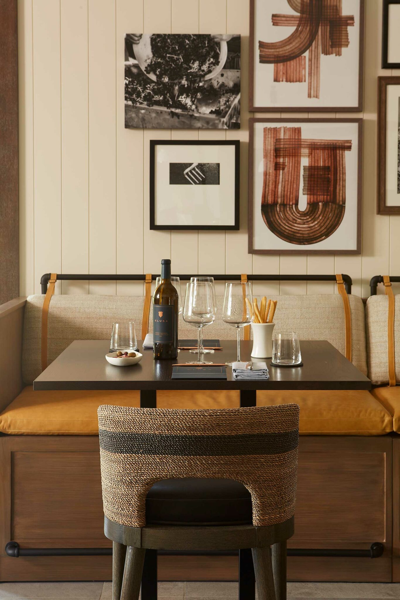 Cozy dining setting of a wine resort with a dark table set for two, featuring wine, glasses, snacks, and modern art on cream walls, creating a warm ambiance.