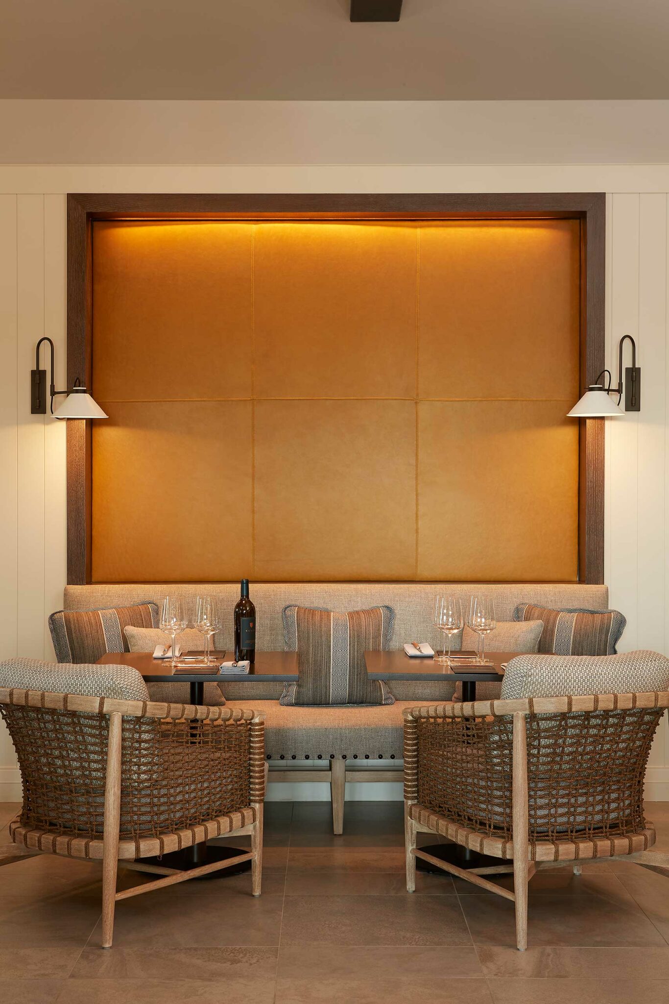 Modern dining area of a winery resort with woven chairs around a wooden table, featuring elegant glassware and a wine bottle. Warm lighting and cozy ambiance.