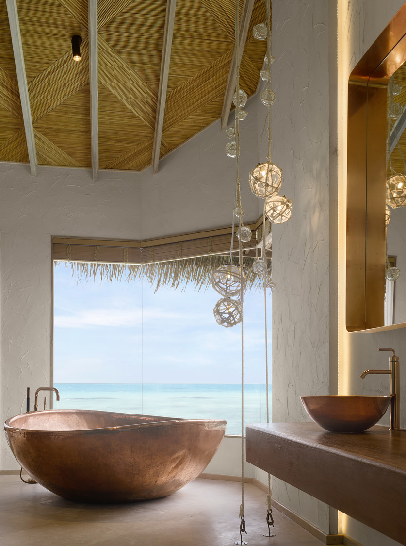 A copper bath in a Maldivian style bathroom of an overwater bungalow style hotel room.