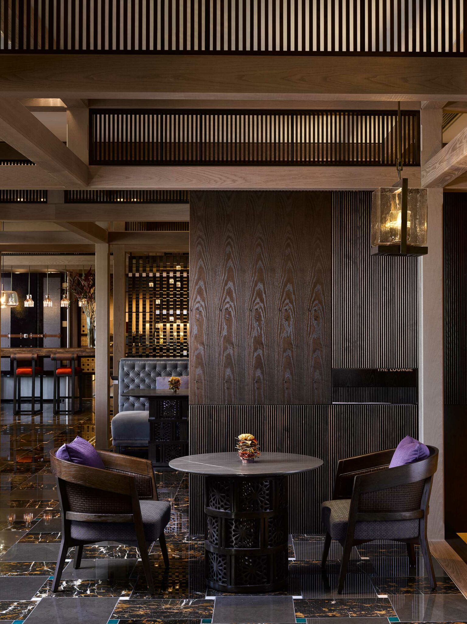 Sophisticated hotel lounge with dark wood accents, plush chairs, and a round table. Warm lighting adds an inviting ambiance. Marble floor enhances elegance.