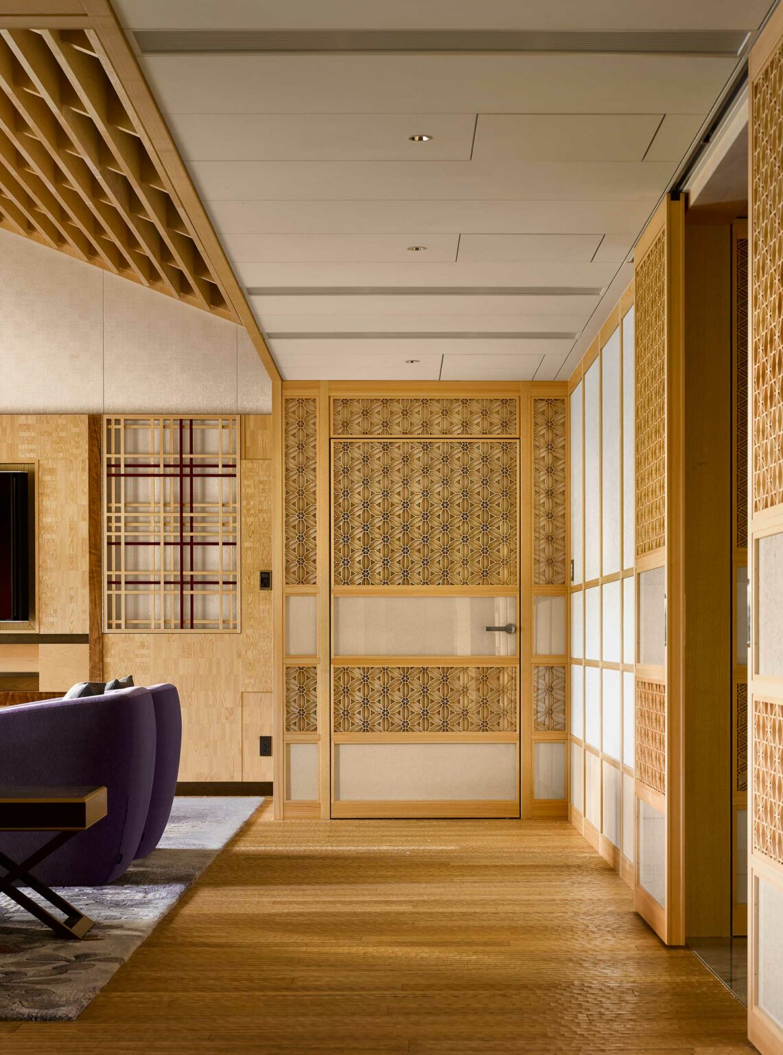 Modern hotel room with Japanese-style design featuring a wooden sliding door with intricate patterns. Warm, neutral tones create a calm, elegant atmosphere.