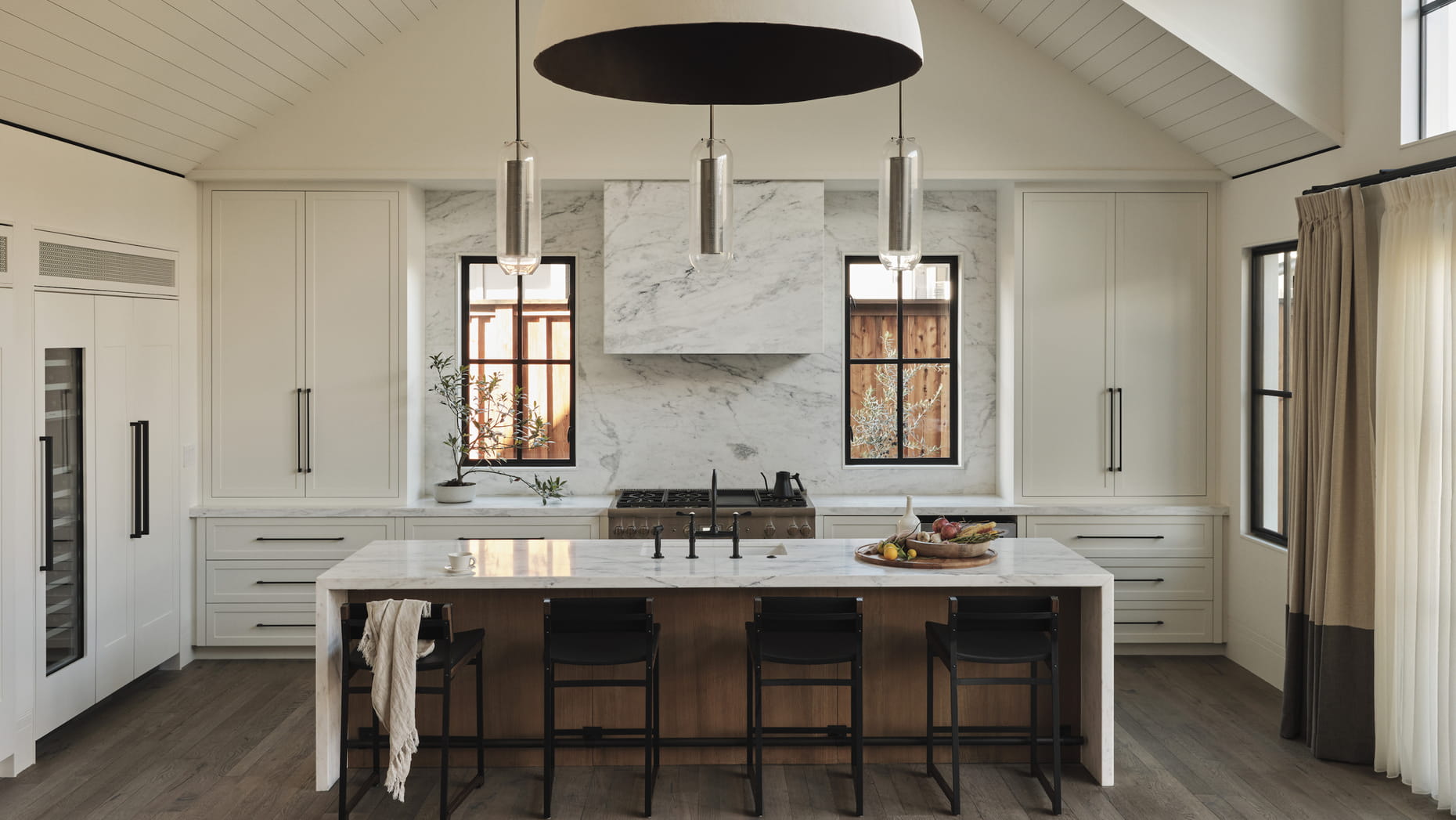 Spacious, modern kitchen of a resort suite with vaulted ceiling, marble counters, and warm lighting. Features include dark bar stools, hanging lights, and large windows.