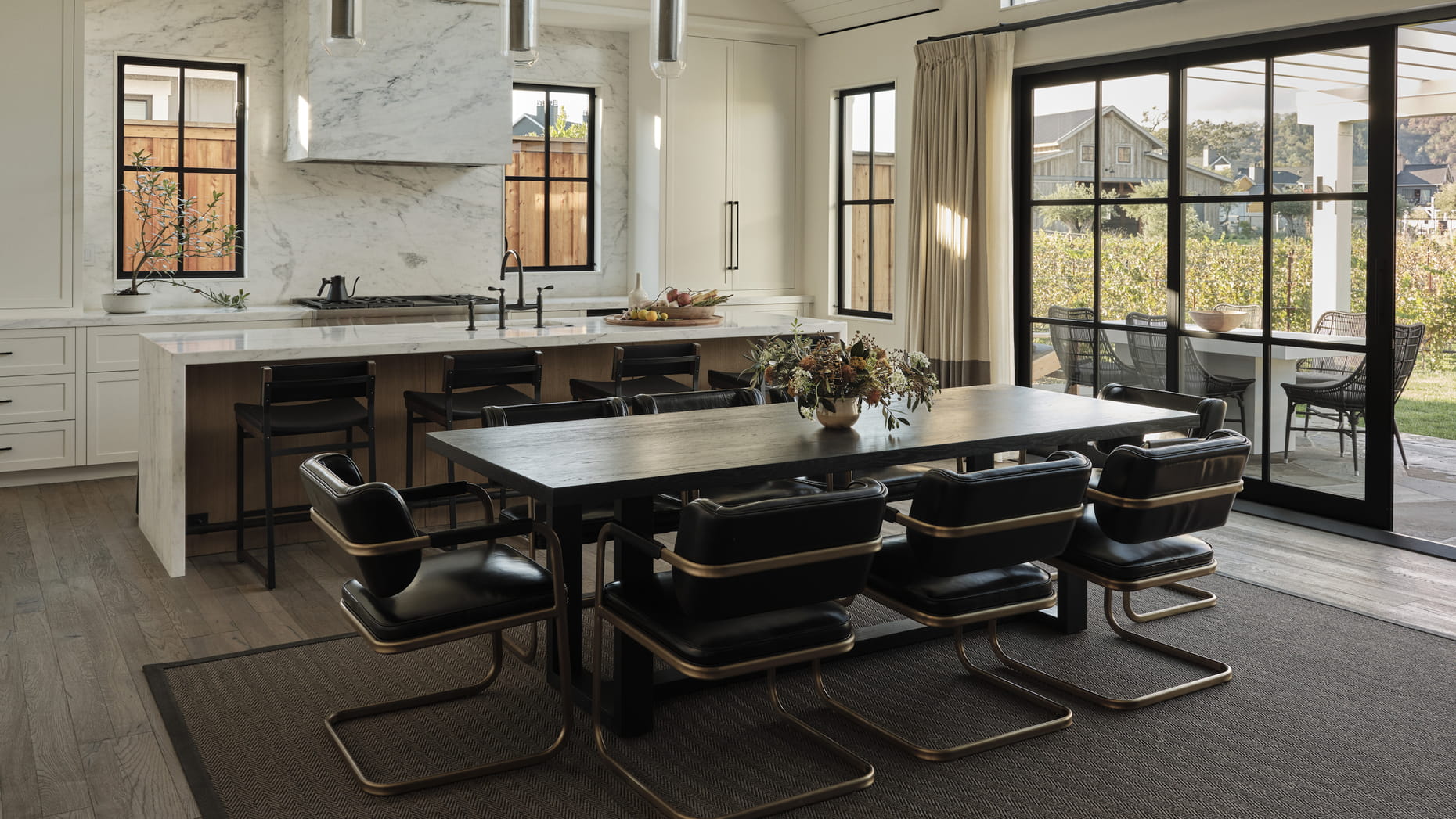 Modern kitchen and dining area of a resort suite with a sleek black dining table, six leather chairs, and a marble kitchen island. Large windows let in natural light.
