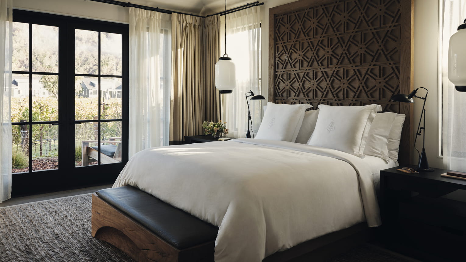 Luxurious resort bedroom with soft bedding and neutral tones, large window showing sunny vineyard view. Elegant and serene atmosphere with cozy ambiance.