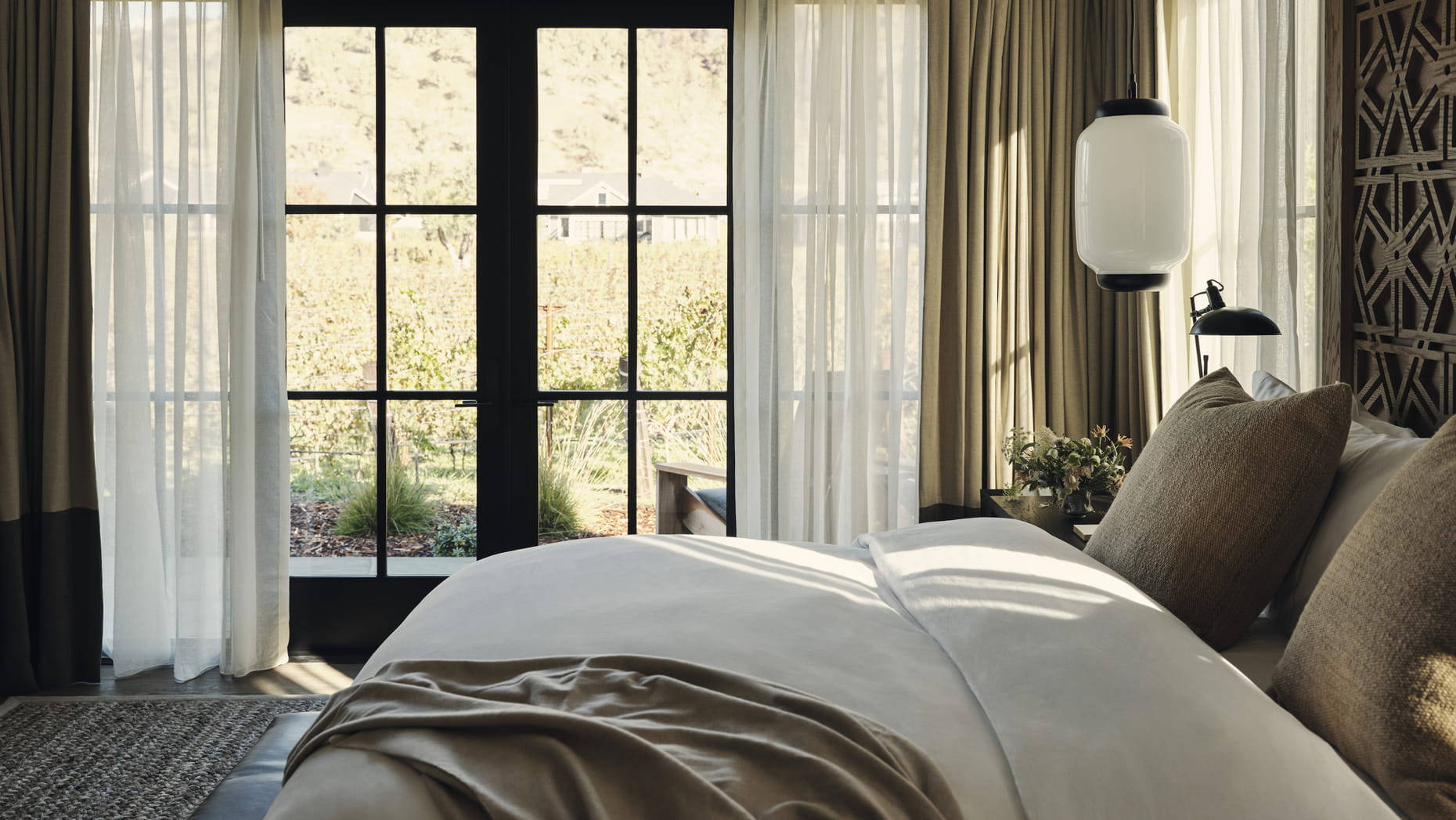 Luxurious resort bedroom with soft bedding and neutral tones, large window showing sunny vineyard view. Elegant and serene atmosphere with cozy ambiance.