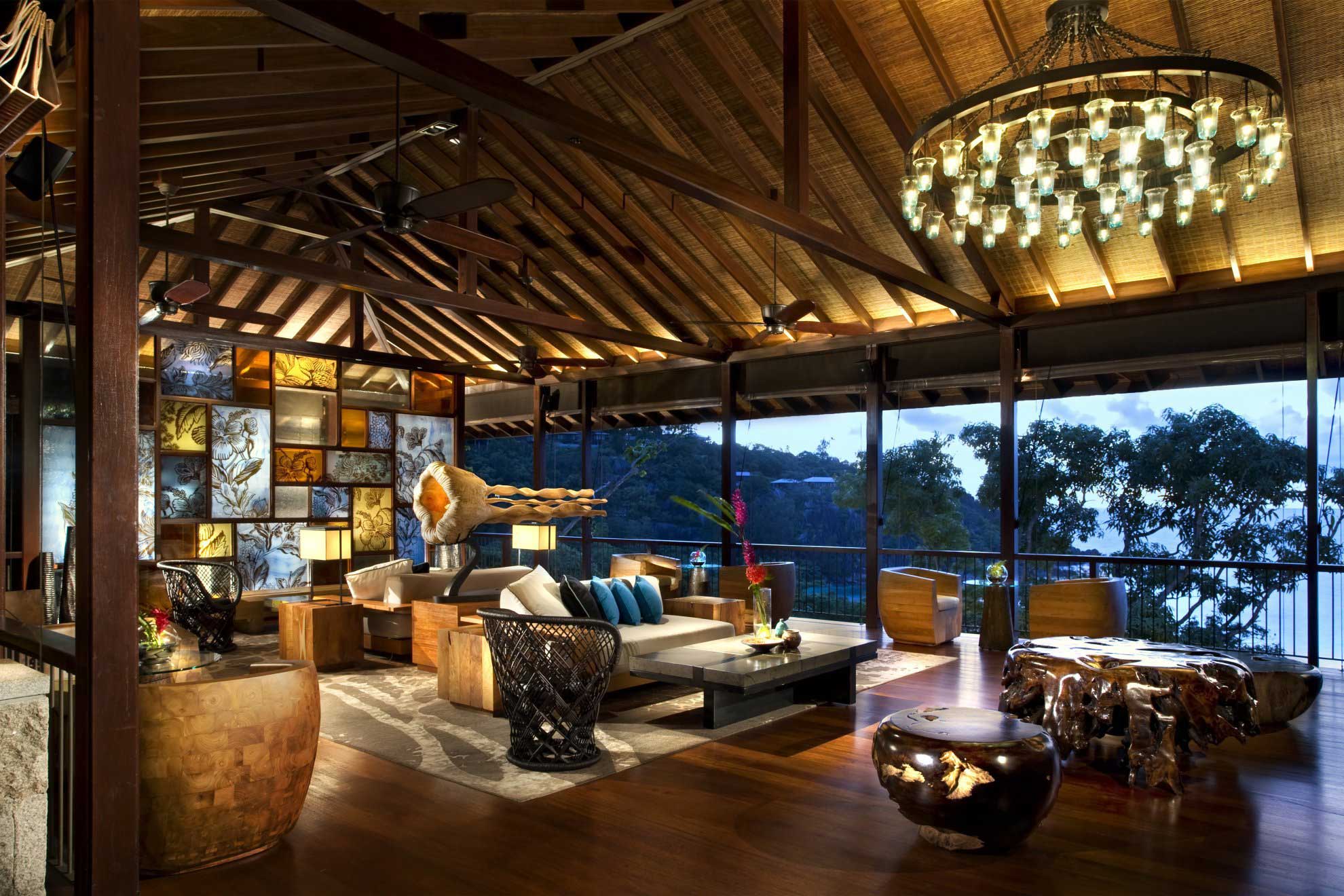 Spacious open-air hotel lounge with rustic wooden ceiling, large chandelier, and vibrant stained glass wall. Cozy sofa and unique sculpted wood tables. Relaxing, artistic atmosphere.