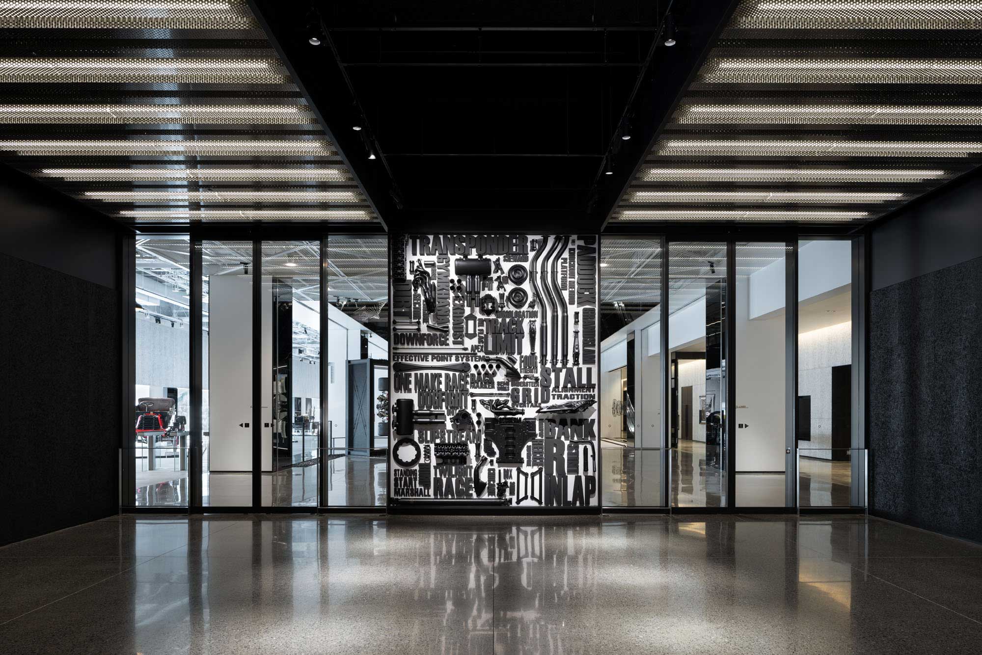 A modern interior with a black and white abstract art mural featuring bold, overlapping text and graphic elements. Reflective flooring and glass walls create an open, contemporary atmosphere.