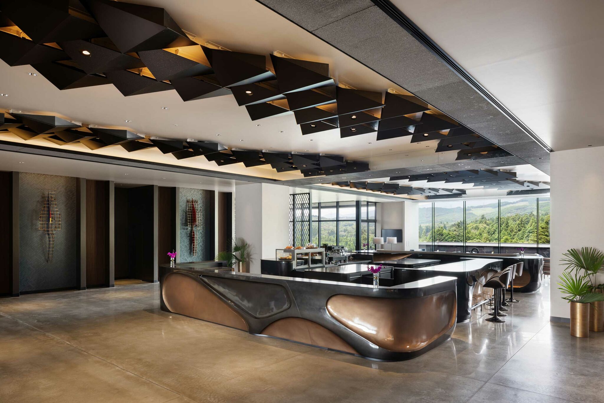 A modern, elegant hotel lobby with a geometric ceiling design, sleek black and bronze furnishings, and large windows revealing a scenic landscape.