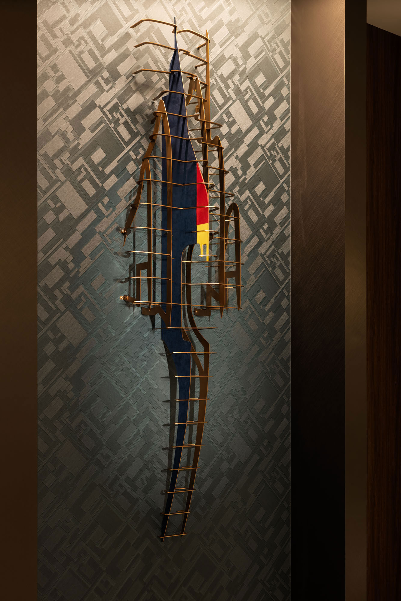 Abstract wall sculpture in a hotel with geometric patterns in the background. A wooden frame outlines a dark blue shape with red and yellow accents, creating a modern, dynamic feel.