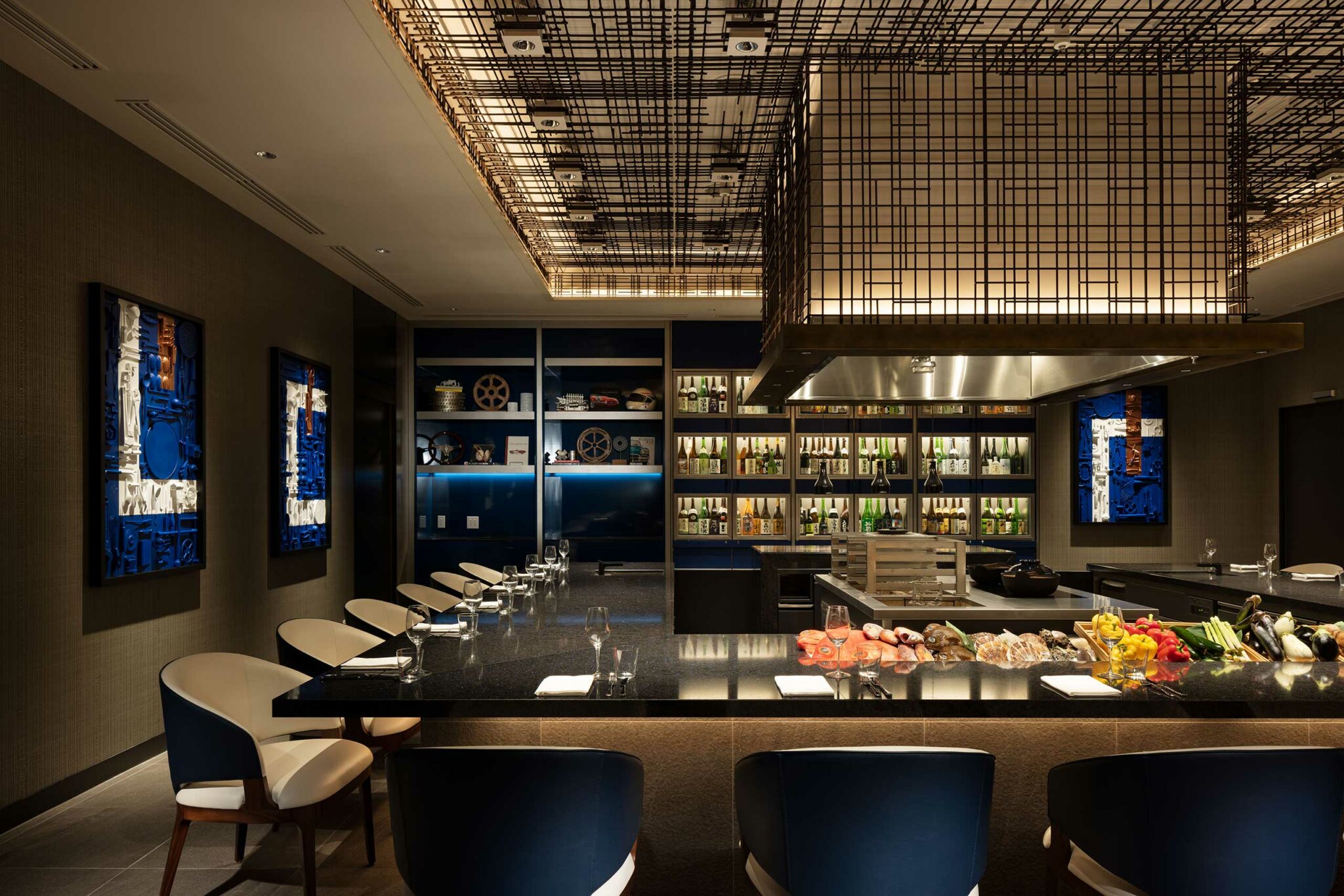 Sophisticated hotel dining area with a sleek black counter, elegant cushioned chairs, decorative wall art, and a well-lit ceiling. Bottles line shelves in the background.