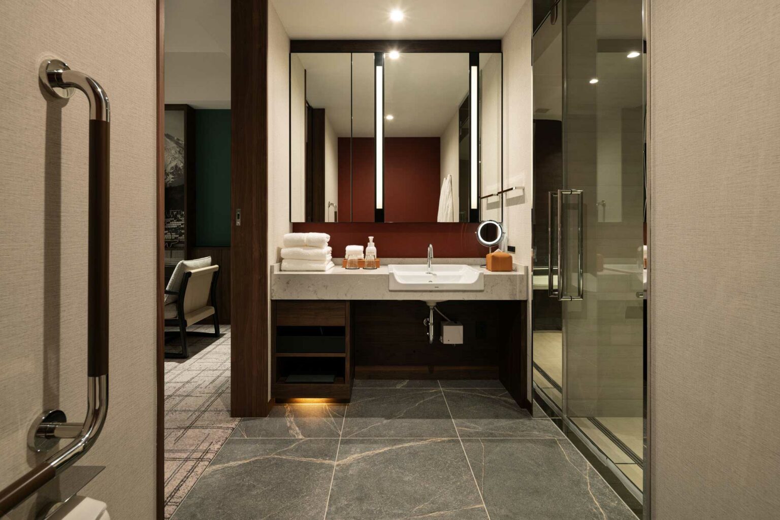 Modern suite bathroom with sleek stone tiles and a large mirror above a countertop sink. Towels and toiletries are neatly arranged, conveying elegance and tidiness.