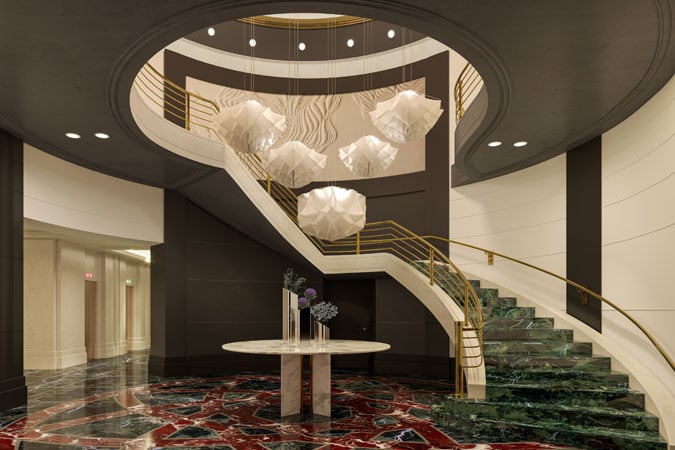 Luxurious hotel lobby with a grand spiral staircase, ornate golden railings, and elegant hanging lights. A round table with flowers adds sophistication.