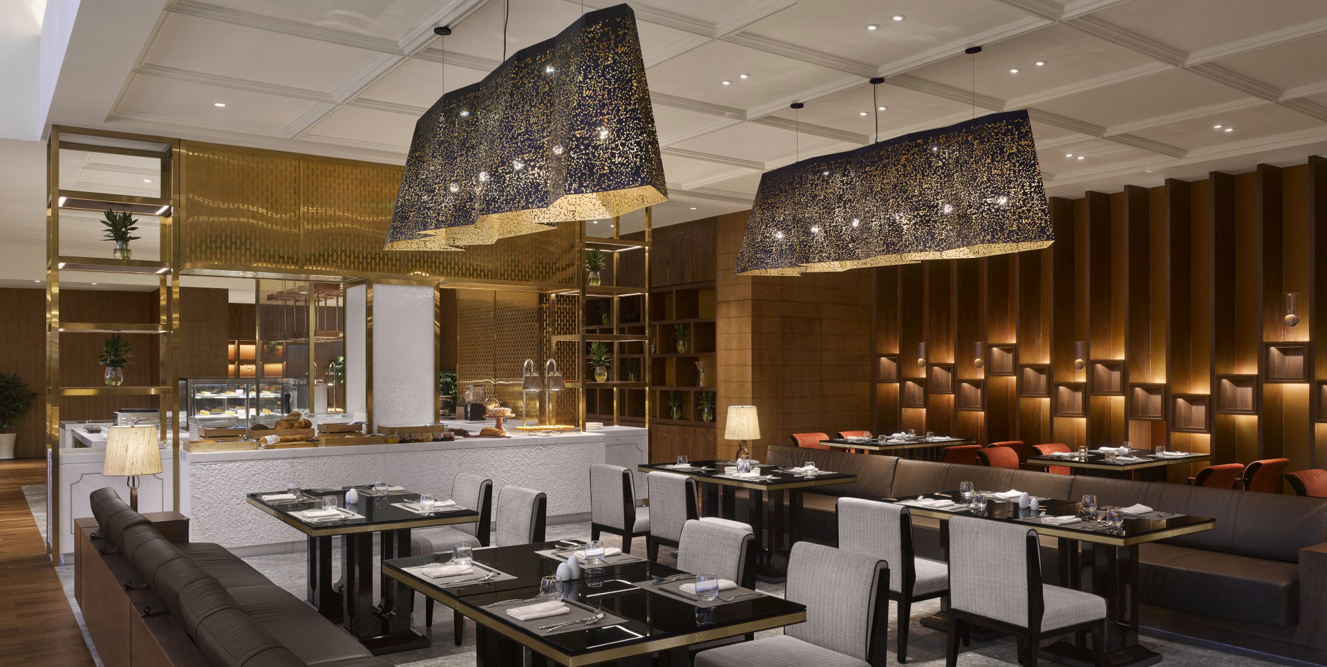 Elegant hotel all day dining area with modern decor, featuring large textured pendant lights, dark tables set with white tableware, and warm wooden accents.