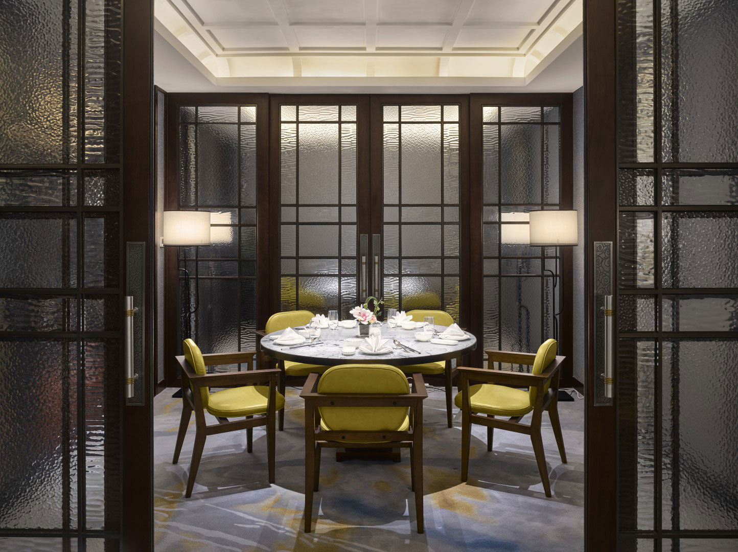 Elegant hotel dining room with a circular table set for four, featuring yellow cushioned chairs and soft lighting, creating a serene and intimate atmosphere.
