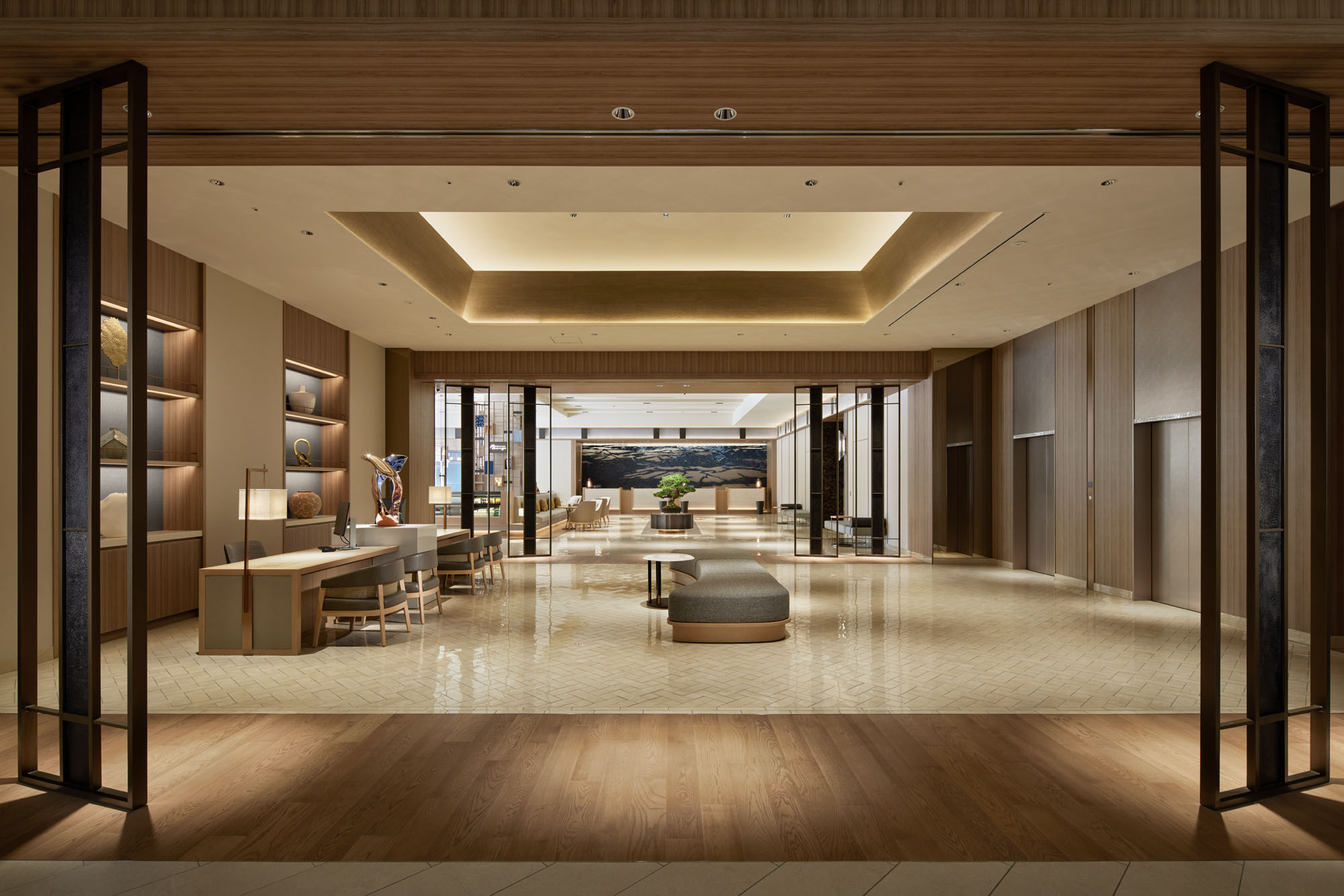 Elegant hotel lobby with warm lighting, modern wooden decor, and beige floors. Cozy seating area and artwork create a welcoming, upscale ambiance.
