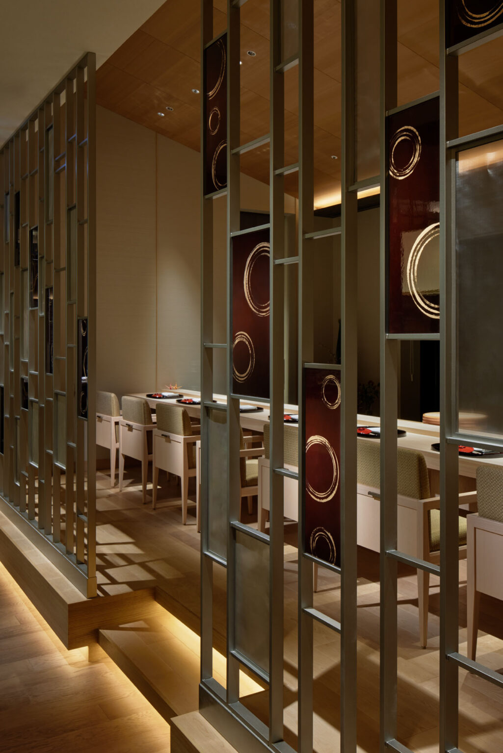 Elegant hotel restaurant interior with a modern partition featuring circular patterns. Soft lighting highlights wooden floors and walls, creating a warm ambiance.