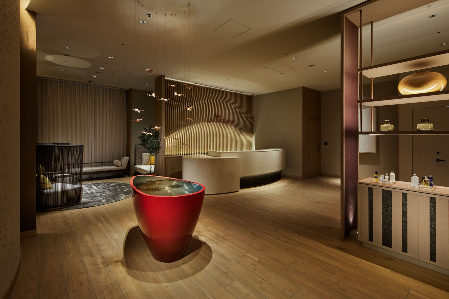 Elegant hotel spa lobby with minimalist decor. Features a red water feature, wooden accents, and soft lighting, creating a tranquil, welcoming atmosphere.