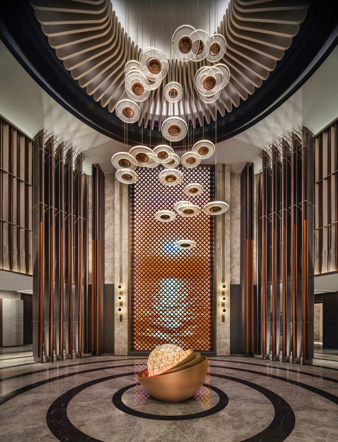 Luxurious hotel lobby with geometric pendant lights, an intricate wood lattice wall, and a central bronze sculpture. Elegant, modern, and inviting ambiance.