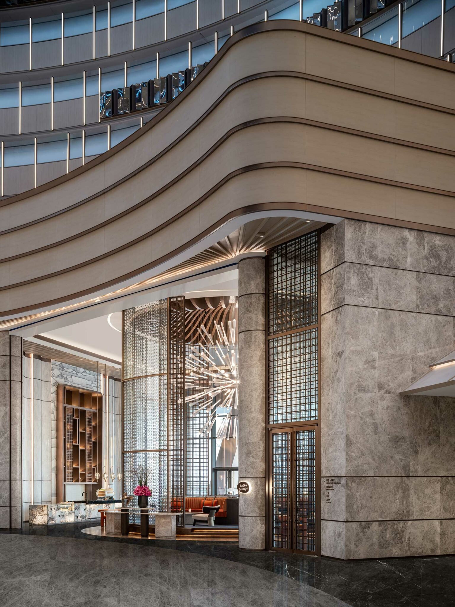 Luxurious hotel lobby with modern design features a striking chandelier, elegant marble pillars, and cozy seating. The atmosphere is sophisticated and welcoming.