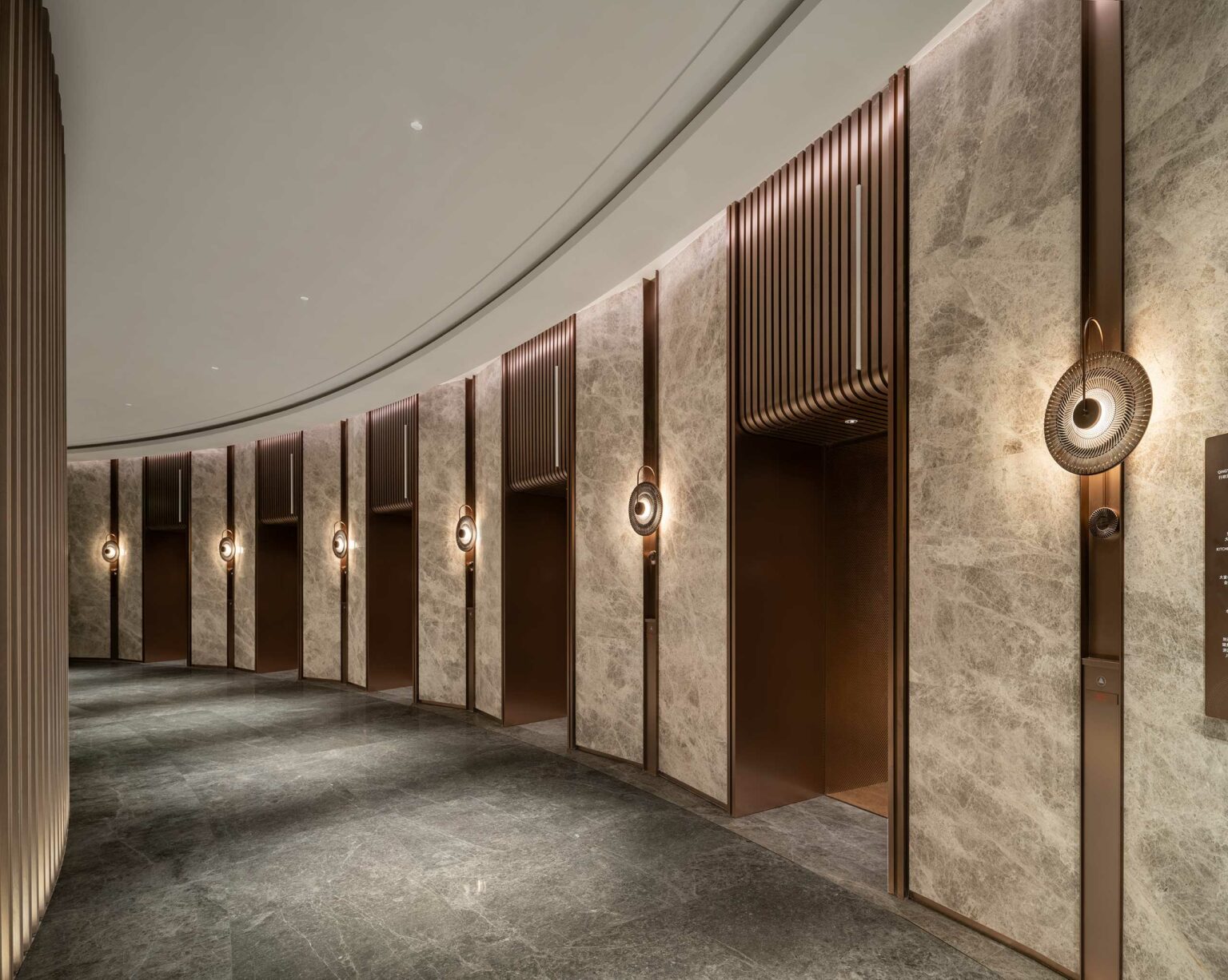 A modern, elegant hotel lift lobby with marble walls, bronze accents, and artistic round sconces, evoking a stylish, serene atmosphere.